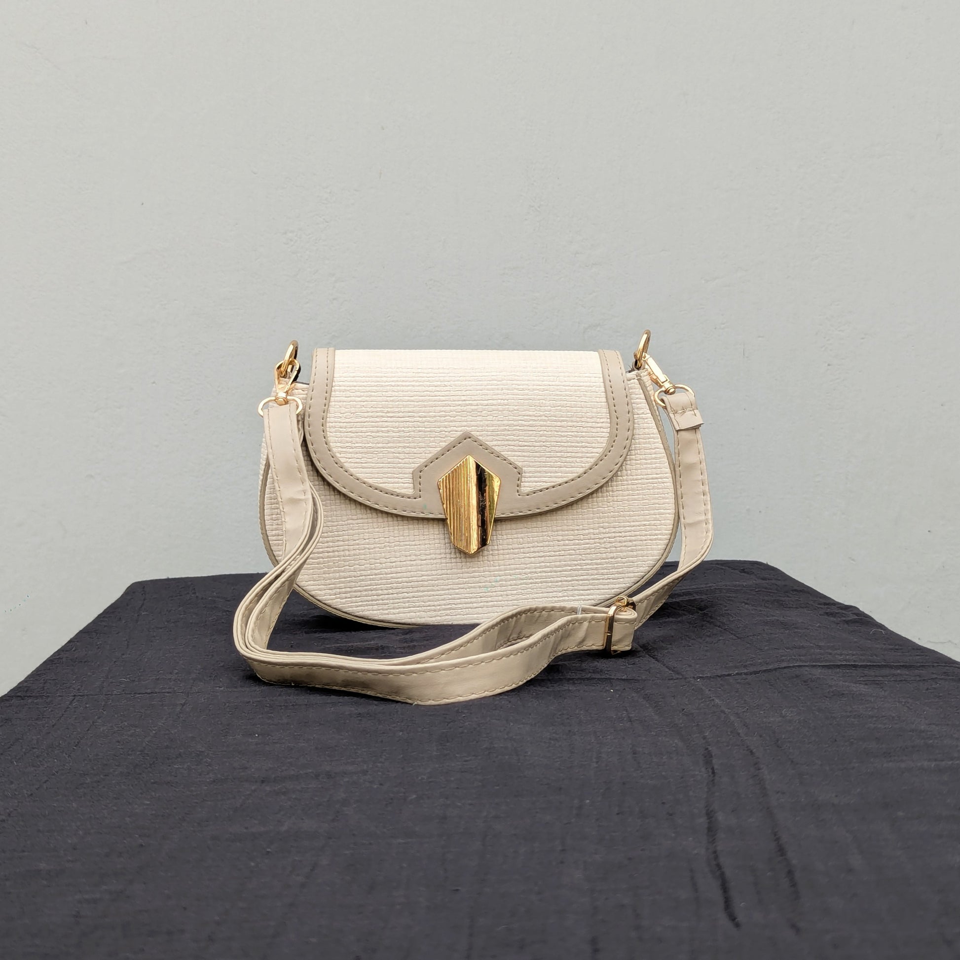 carinno.shop brings you the perfect small beige crossbody bag with a woven-like texture, golden logo-free clasp, golden hardware, and an adjustable strap, placed on a black surface.