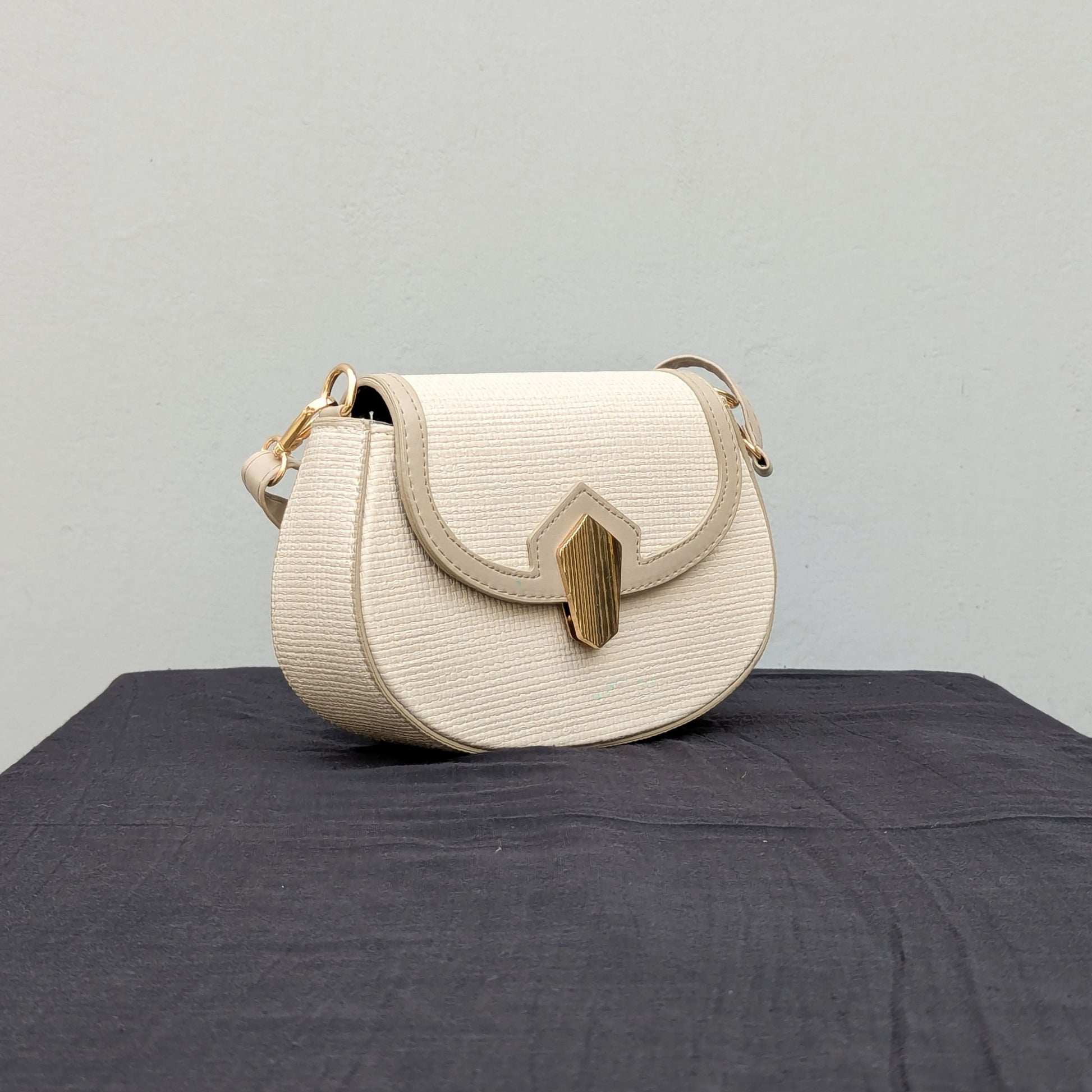 carinno.shop brings you the perfect small beige crossbody bag with a woven-like texture, golden logo-free clasp, golden hardware, and an adjustable strap, placed on a black surface.